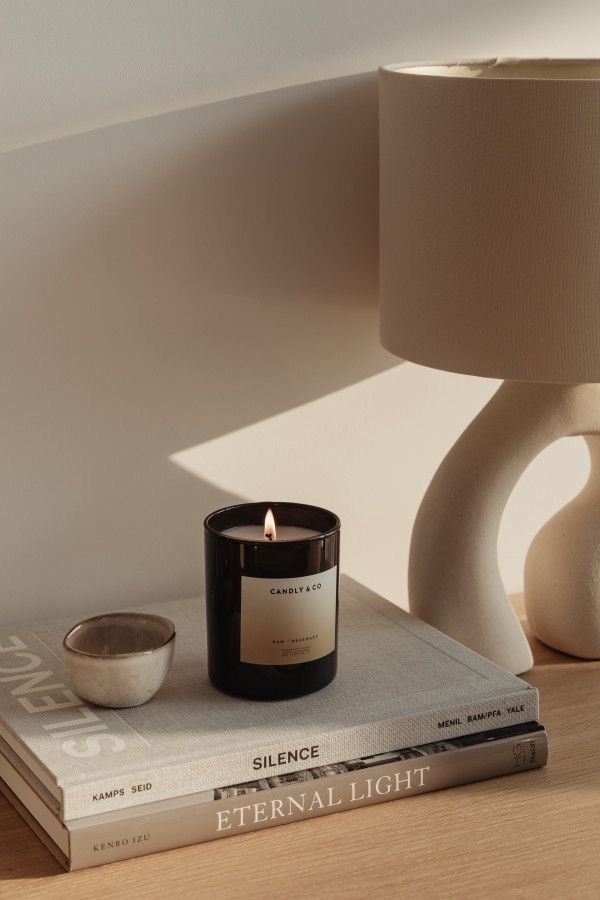 Warm, minimalist vignette featuring a lit candle, ceramic lamp, and stacked books on a wooden table.
