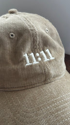 Angled view of a beige corduroy hat featuring white 11:11 embroidery.