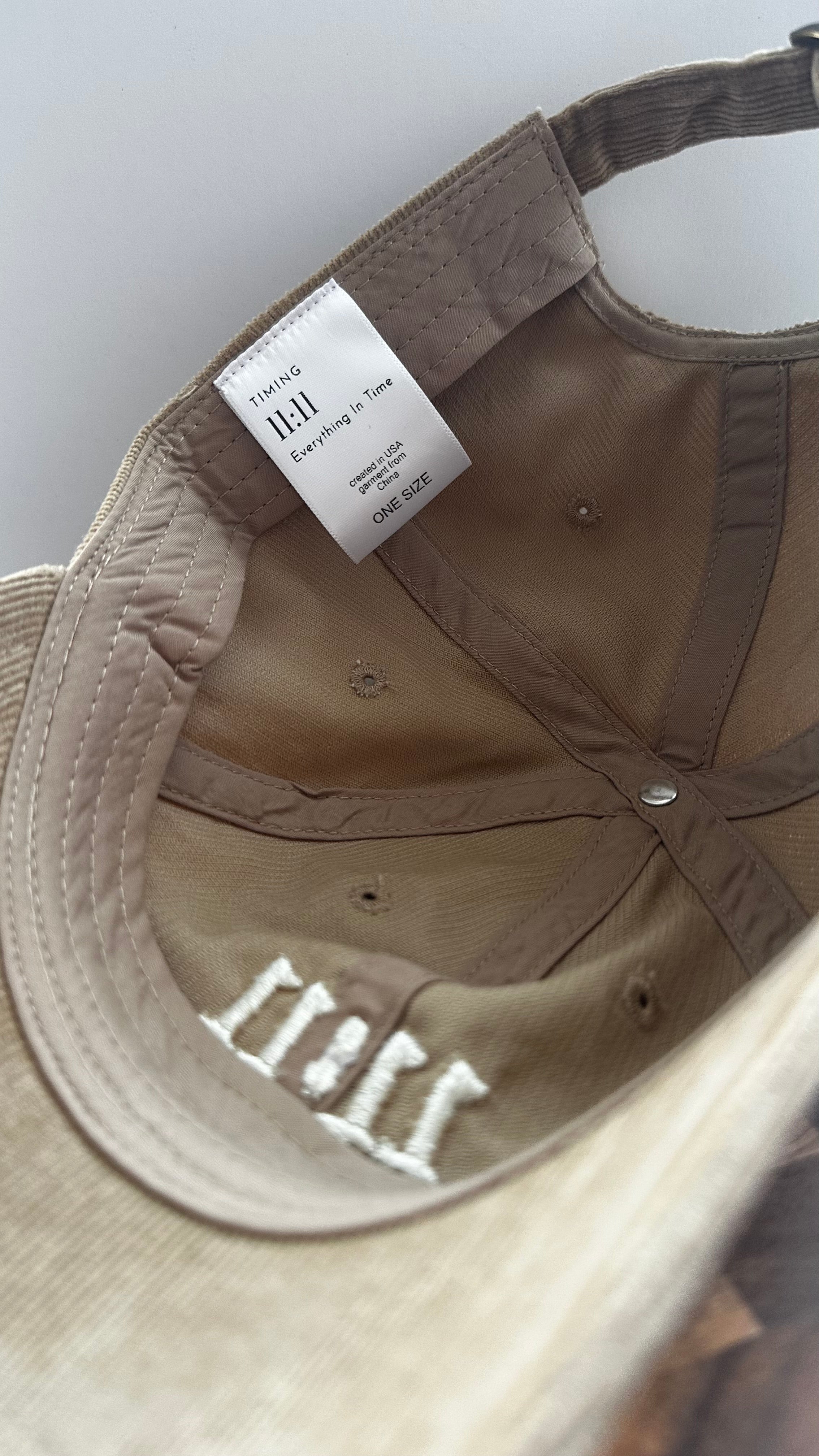 Interior view of a beige corduroy hat featuring the Timing 11:11 signature label and embroidered 11:11 design.
