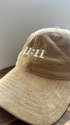 Angled view of a beige corduroy hat featuring white 11:11 embroidery.