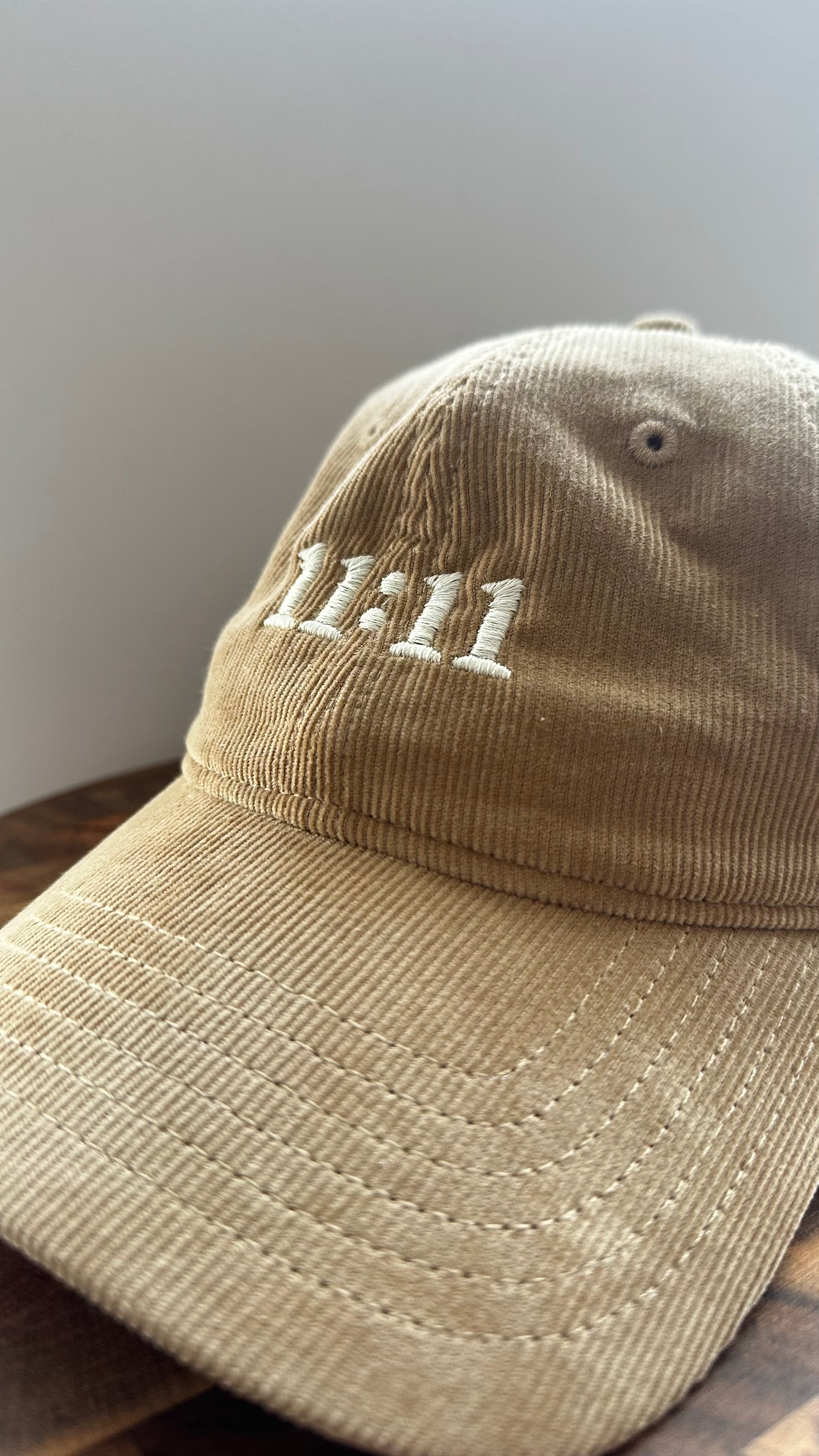 Angled view of a beige corduroy hat featuring white 11:11 embroidery.