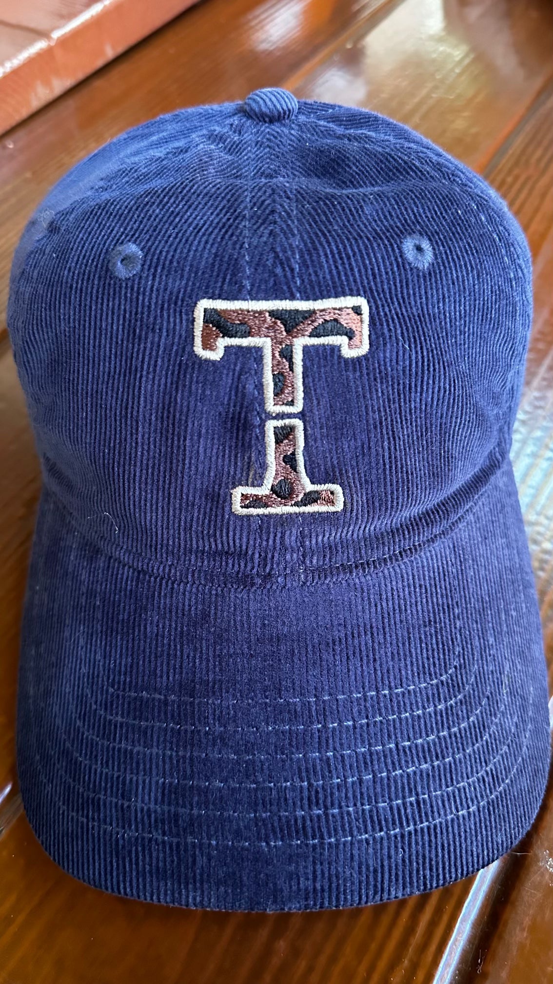 Navy corduroy cap featuring an embroidered, interrupted Threshold T in leopard print with a cream outline, shown from the front.