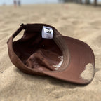 Interior view of a brown dad hat resting on the sand at the beach
