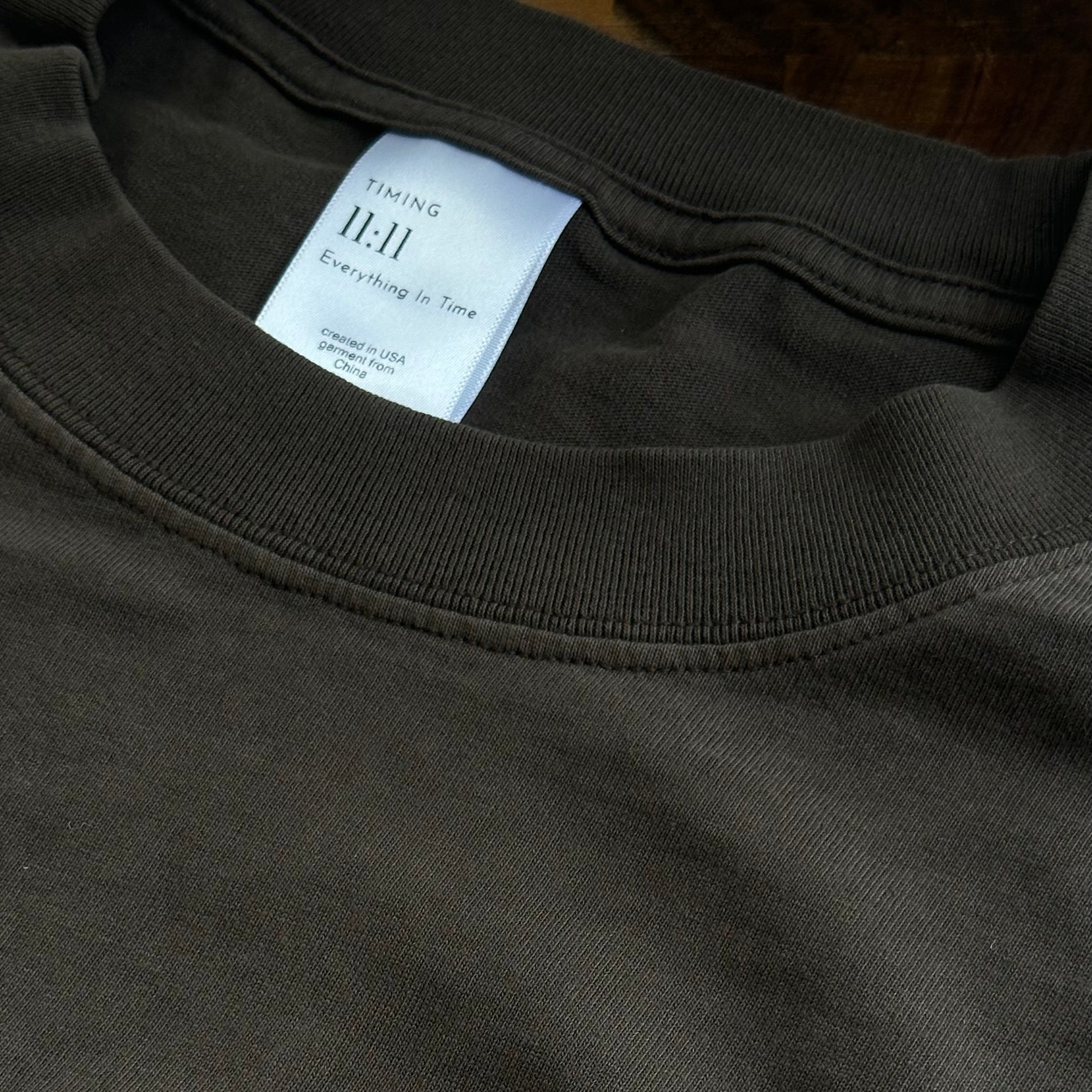 Close-up of the Timing 11:11 signature label and ribbed collar on a brown t-shirt.