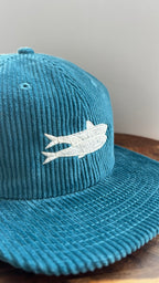 Close-up showcasing the corduroy texture and embroidered sardine design on a teal hat
