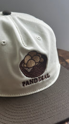 Angled close-up of a cream and brown two-tone cap with embroidered basket of pandesal and "PANDESAL" text.