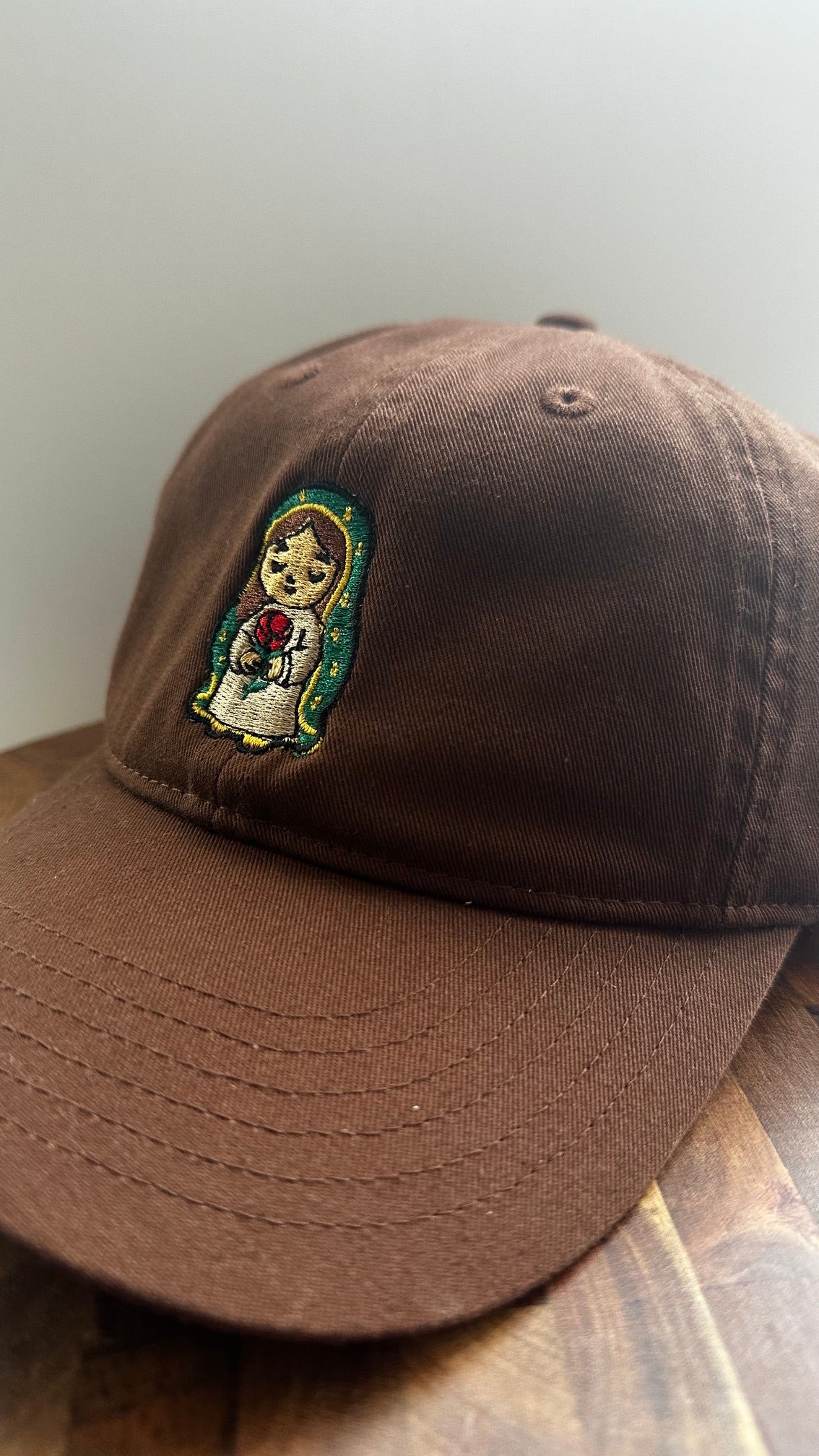 Angled view of a brown dad hat featuring embroidered Rose Protector holding a red rose.
