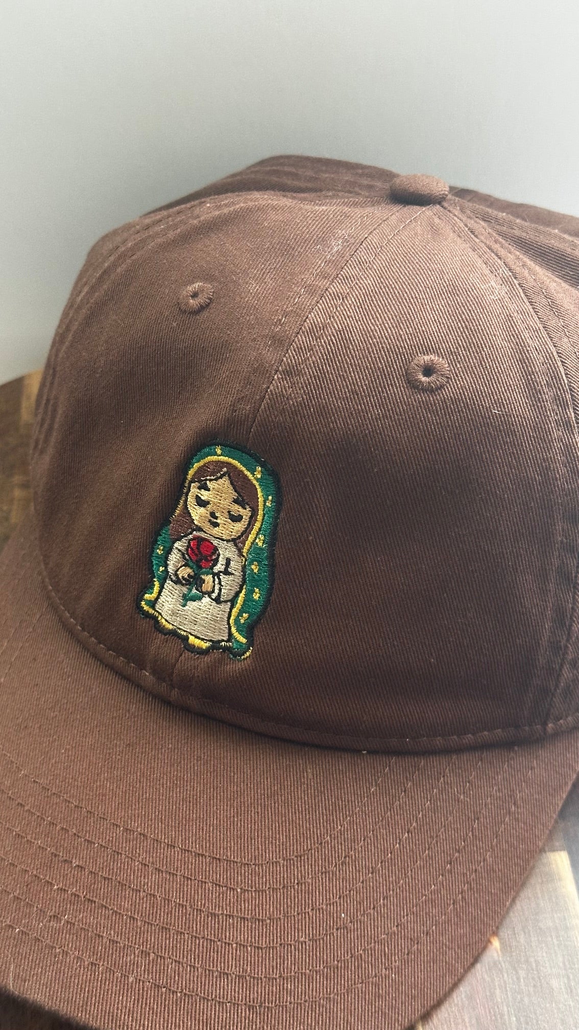 Angled front view of a brown dad hat featuring embroidered Rose Protector holding a red rose.