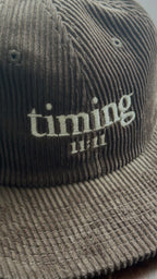 Close-up showcasing the corduroy texture and embroidered "timing 11:11" logo on a brown hat