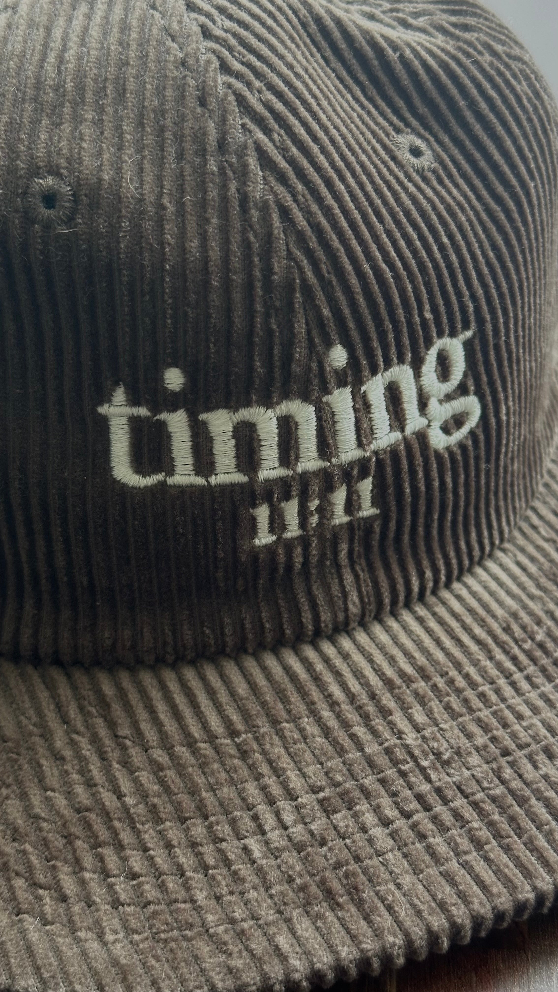 Close-up showcasing the corduroy texture and embroidered "timing 11:11" logo on a brown hat