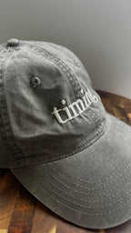 Angled view of a vintage washed gray dad hat featuring ivory "timing" embroidery.