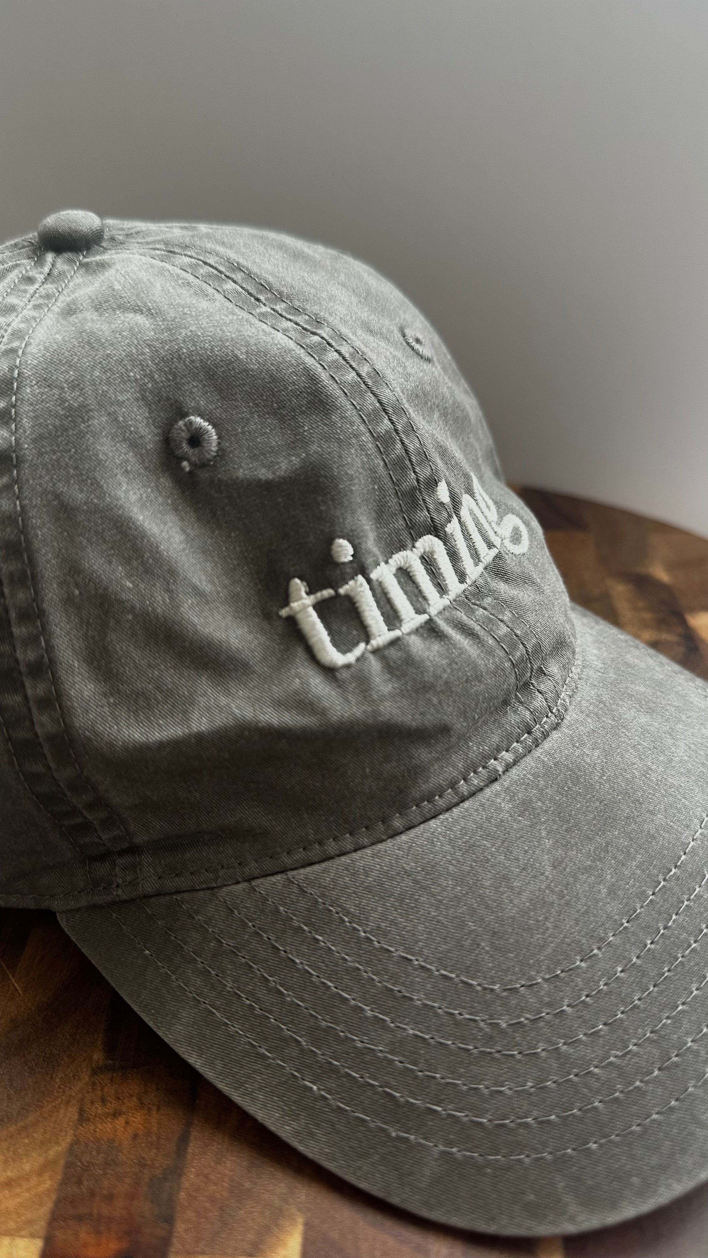 Angled view of a vintage washed gray dad hat featuring ivory "timing" embroidery.
