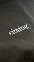 Brown fabric with white embroidered text 'timing'