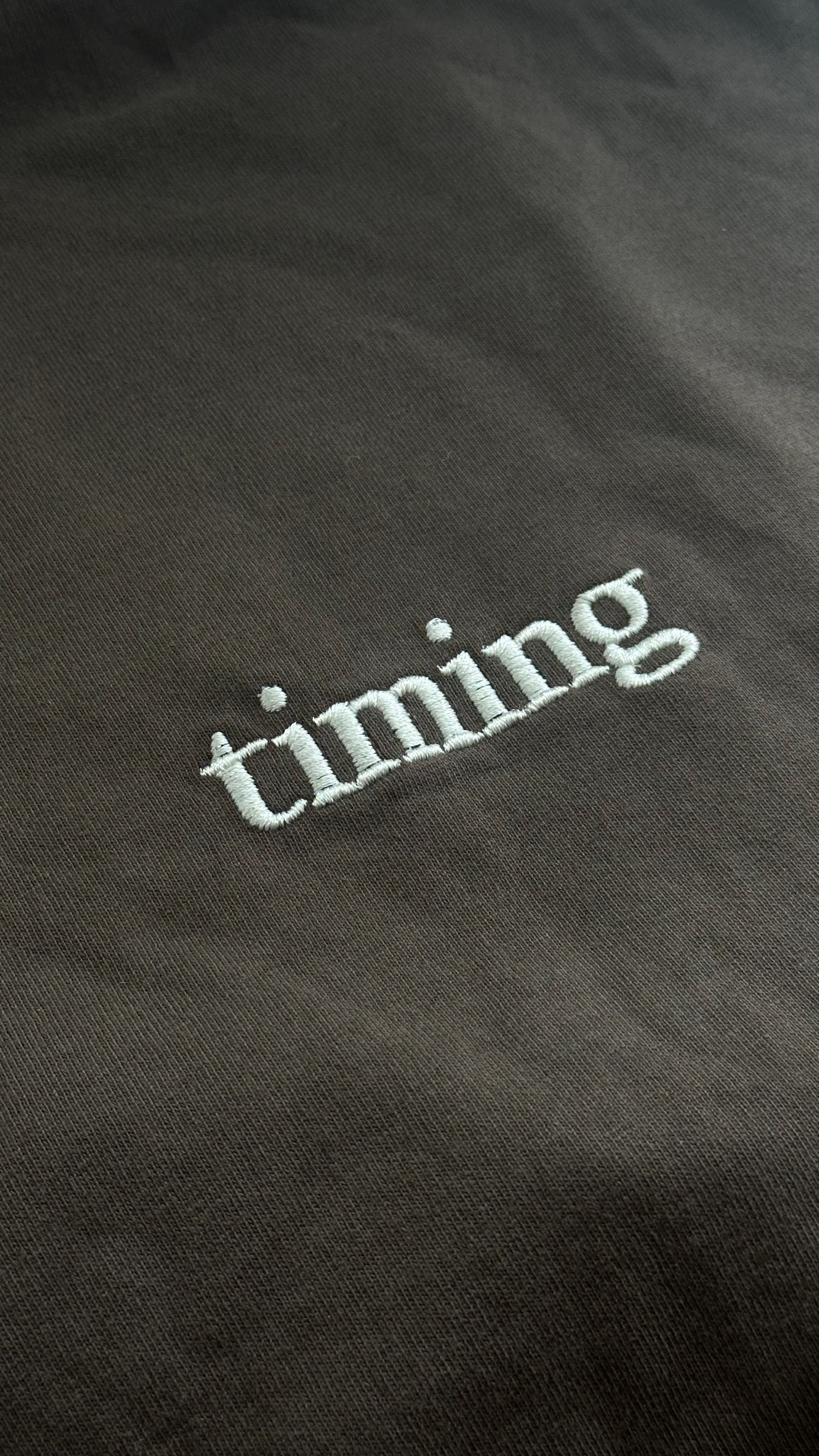 Brown fabric with white embroidered text 'timing'