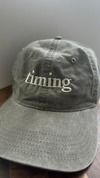 Front view of a vintage washed gray dad hat featuring ivory "timing" embroidery.