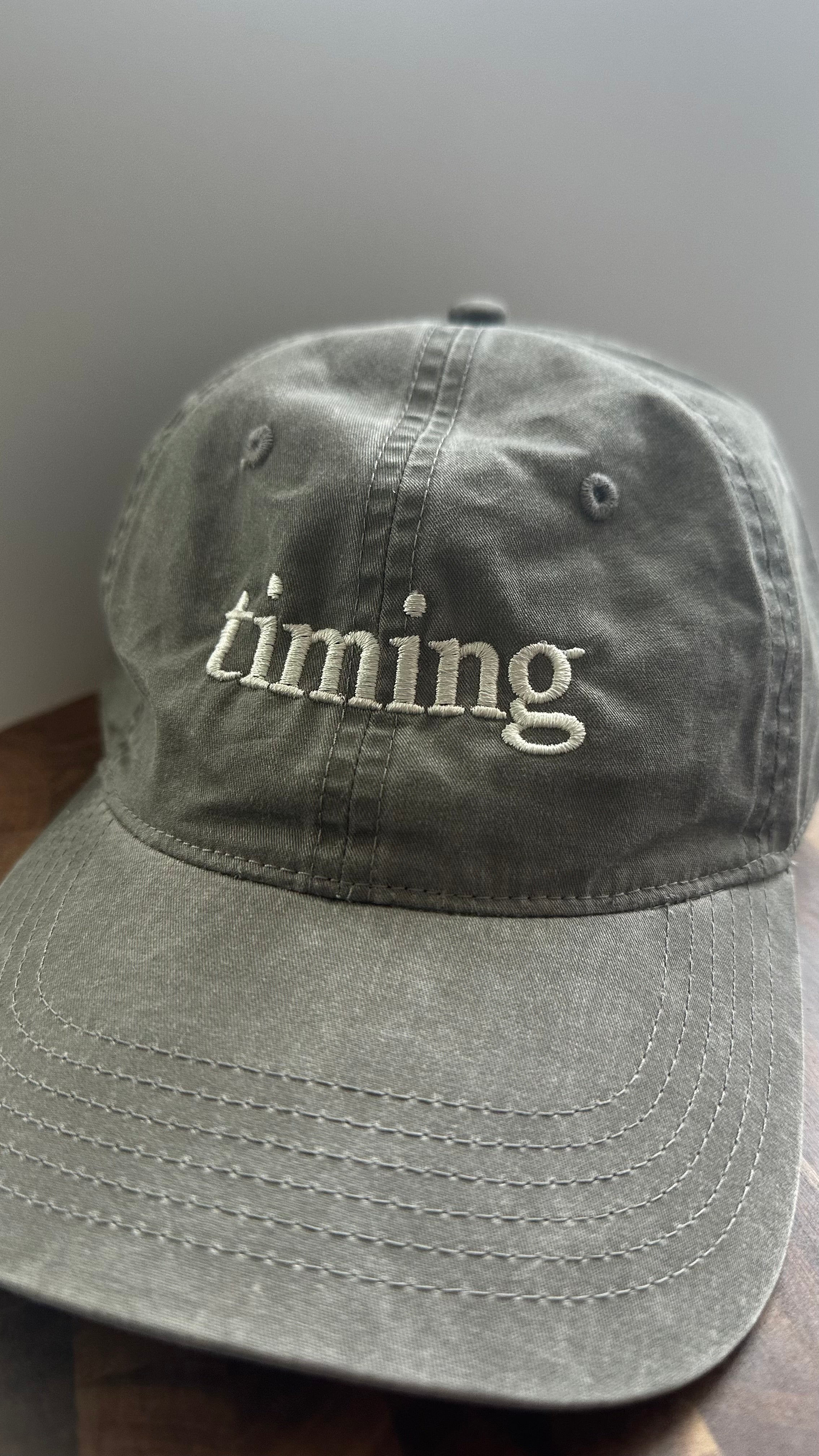 Front view of a vintage washed gray dad hat featuring ivory "timing" embroidery.