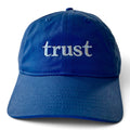 Blue organic cotton dad hat with "trust." embroidered in warm ivory serif lettering on the front.