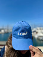 Blue trust embroidered cap worn outdoors by a marina