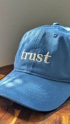 Three-quarter view of the Timing 11:11 Trust cotton dad hat in still water blue with cream embroidered "trust." lettering.