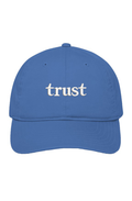 Blue organic cotton dad hat with "trust." embroidered in warm ivory serif lettering on the front.