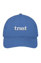 Blue organic cotton dad hat with "trust." embroidered in warm ivory serif lettering on the front.
