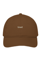 Brown organic cotton dad hat with "trust." embroidered in warm ivory serif lettering on the front.