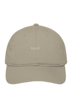 Light cream organic cotton dad hat with "trust." embroidered in warm ivory serif lettering on the front.